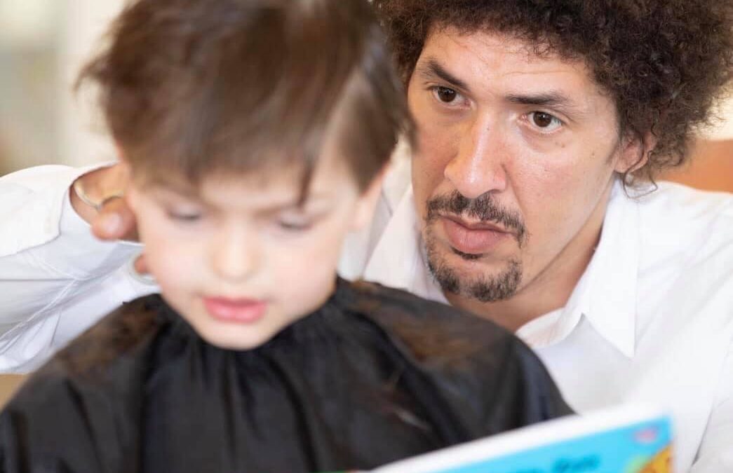 Vorlesefrisör Danny Beuerbach schneidet Kind die Haare, während es vorliest